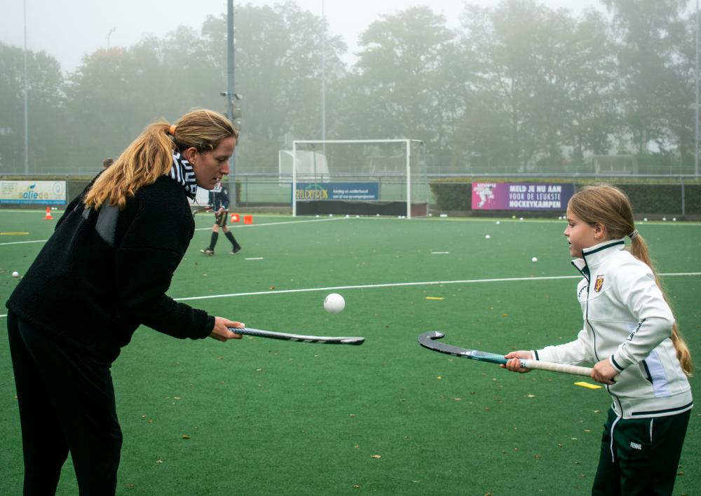 Een volwassene en een kind met hockeysticks bij het hockeyveld